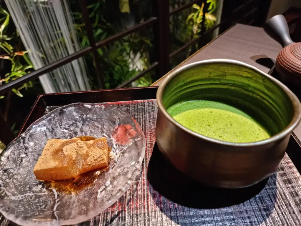 A serving of traditional warabi mochi with kinako powder next to a rich bowl of matcha tea at Saryo Suisen Kyoto.