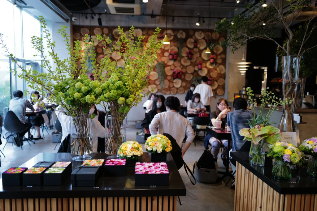 The bustling cafe area at Nicolai Bergmann NOMU, with patrons enjoying the atmosphere surrounded by floral decor.