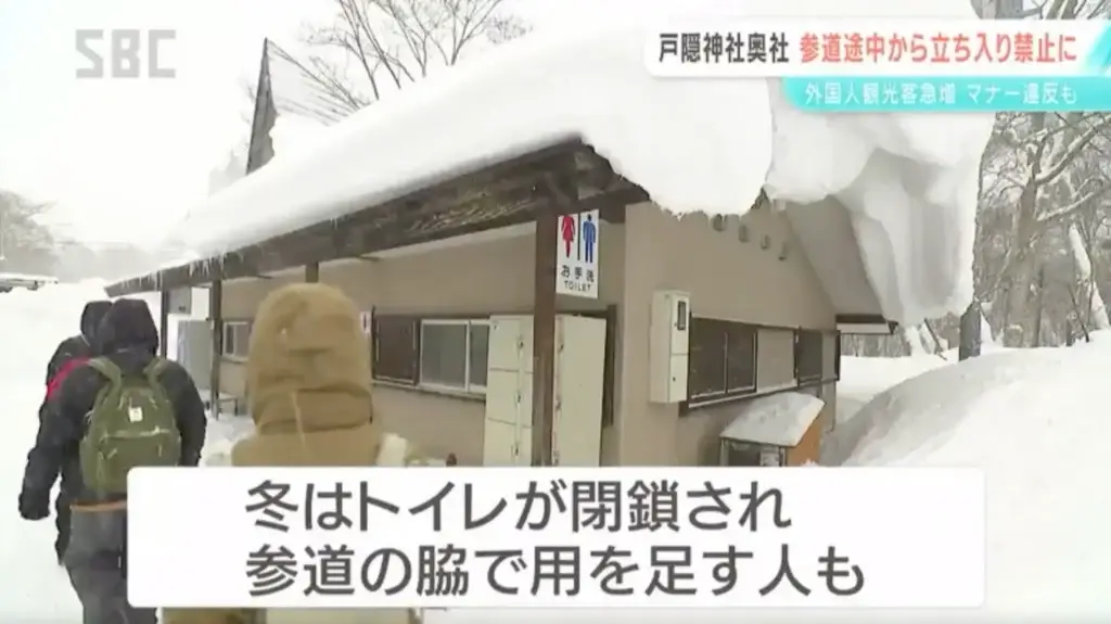 Closed public toilet at Togakushi Shrine in winter, with visitors walking past in the snow.
