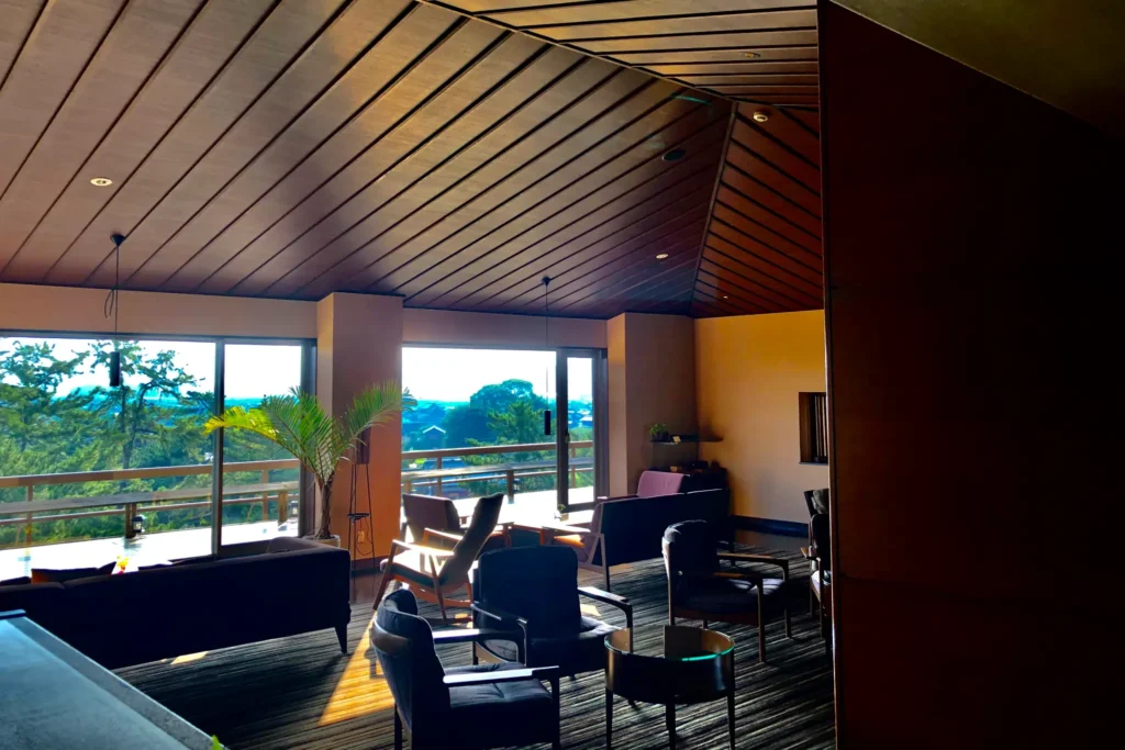 The lounge at Kotohira Kadan ryokan in Kagawa, featuring a modern wooden ceiling design and panoramic windows overlooking the Japanese garden where guests can enjoy a welcome drink.