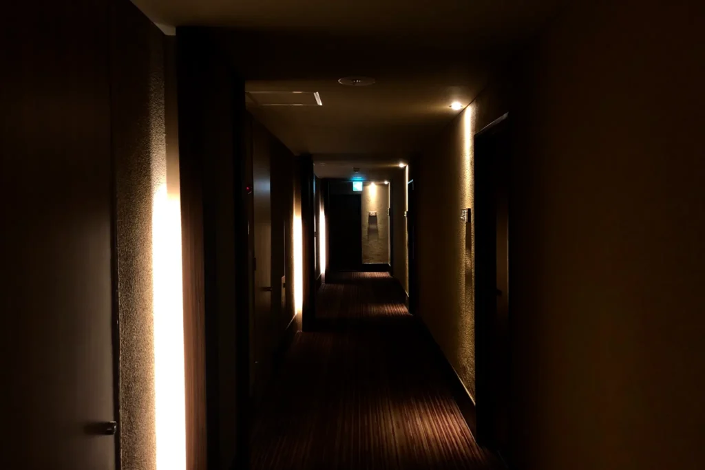 A dimly lit corridor at Kotohira Kadan ryokan with warm ambient lighting and dark wood flooring, creating an atmosphere of quiet elegance.