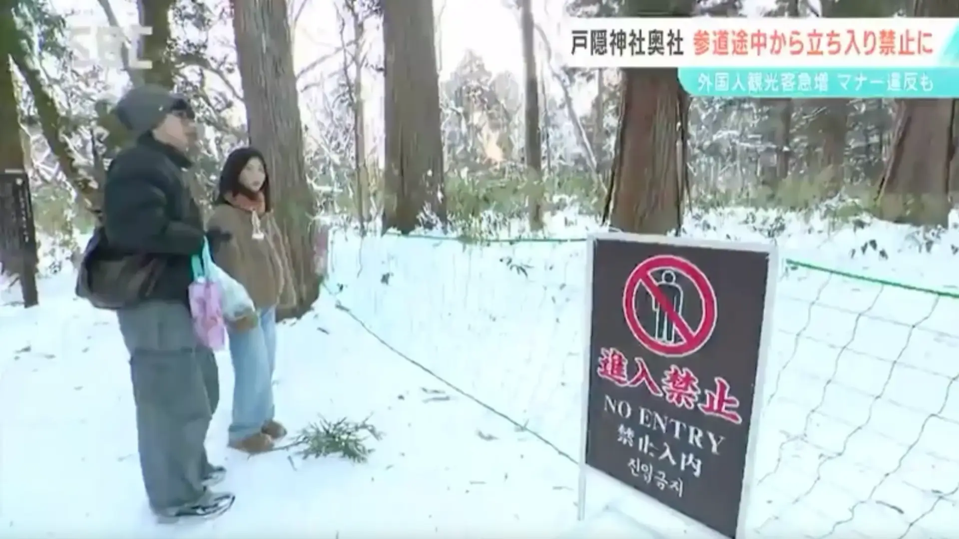 No Entry sign in multiple languages at Togakushi Shrine's cedar avenue, with visitors standing in front of the barrier net in winter.