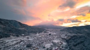 A stunning aerial view of a snow-covered town at the base of Mt. Fuji during a dramatic winter sunrise, illustrating the beauty of Mt Fuji snow.