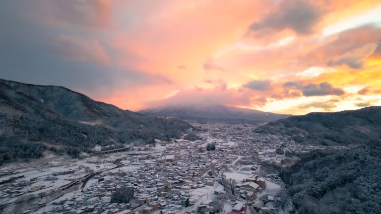 A stunning aerial view of a snow-covered town at the base of Mt. Fuji during a dramatic winter sunrise, illustrating the beauty of Mt Fuji snow.