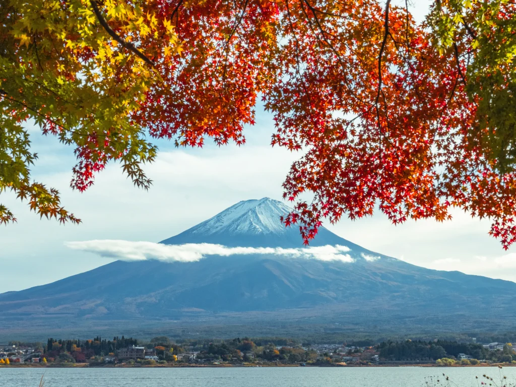 Mt. Fuji framed by vibrant red and yellow autumn maple leaves at Lake Kawaguchiko, with a band of cloud around the mountain — the best time to see Mt Fuji in autumn.