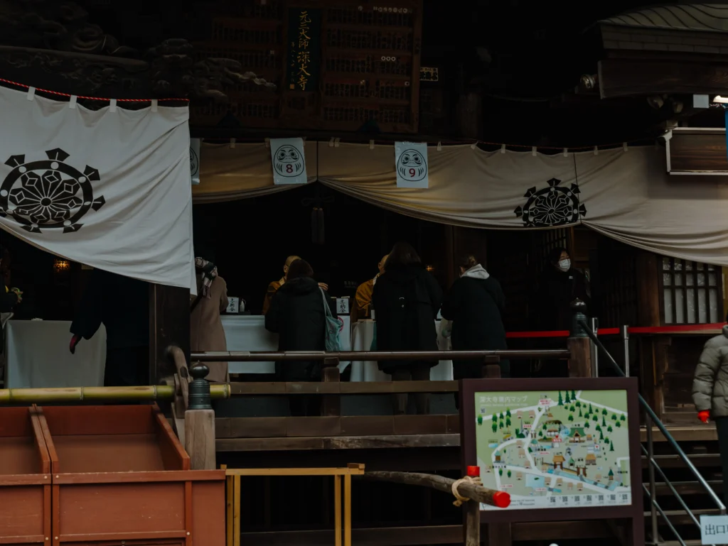Visitors line up at the me-ire station at the Jindaiji Daruma Ichi to have a monk paint the eye of their new daruma doll.