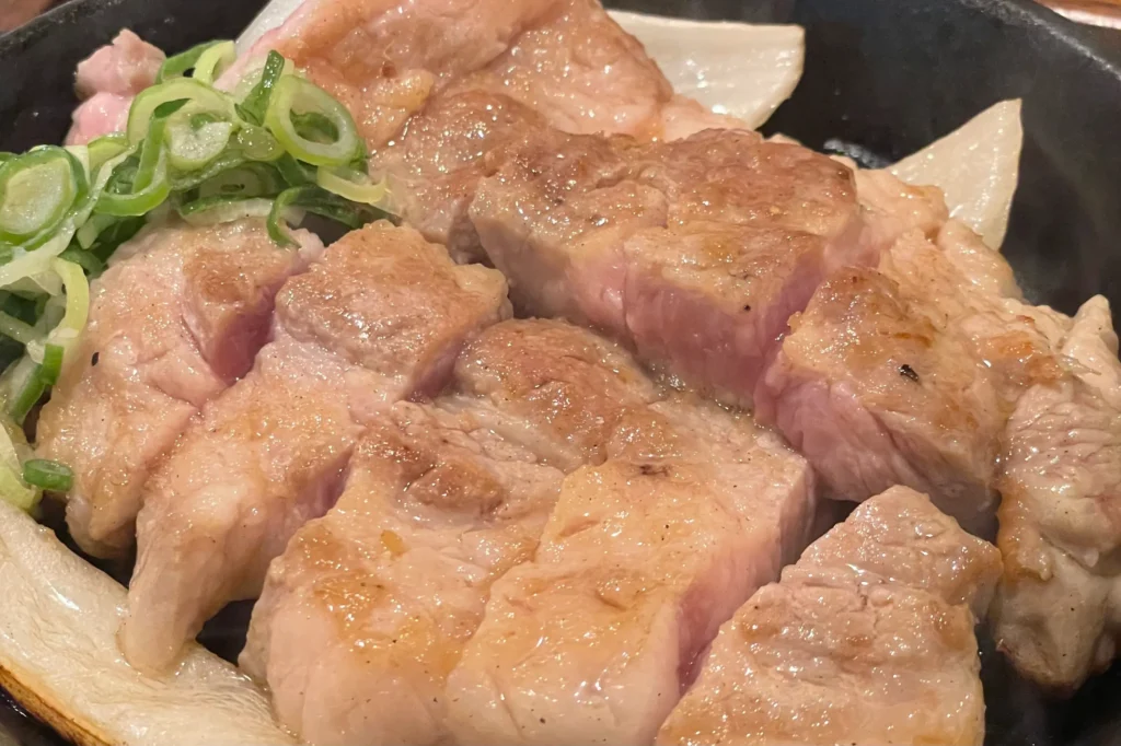 Close-up of the Toichi pork steak Fukuoka, showing the juicy, medium-rare pink center on a sizzling teppan.