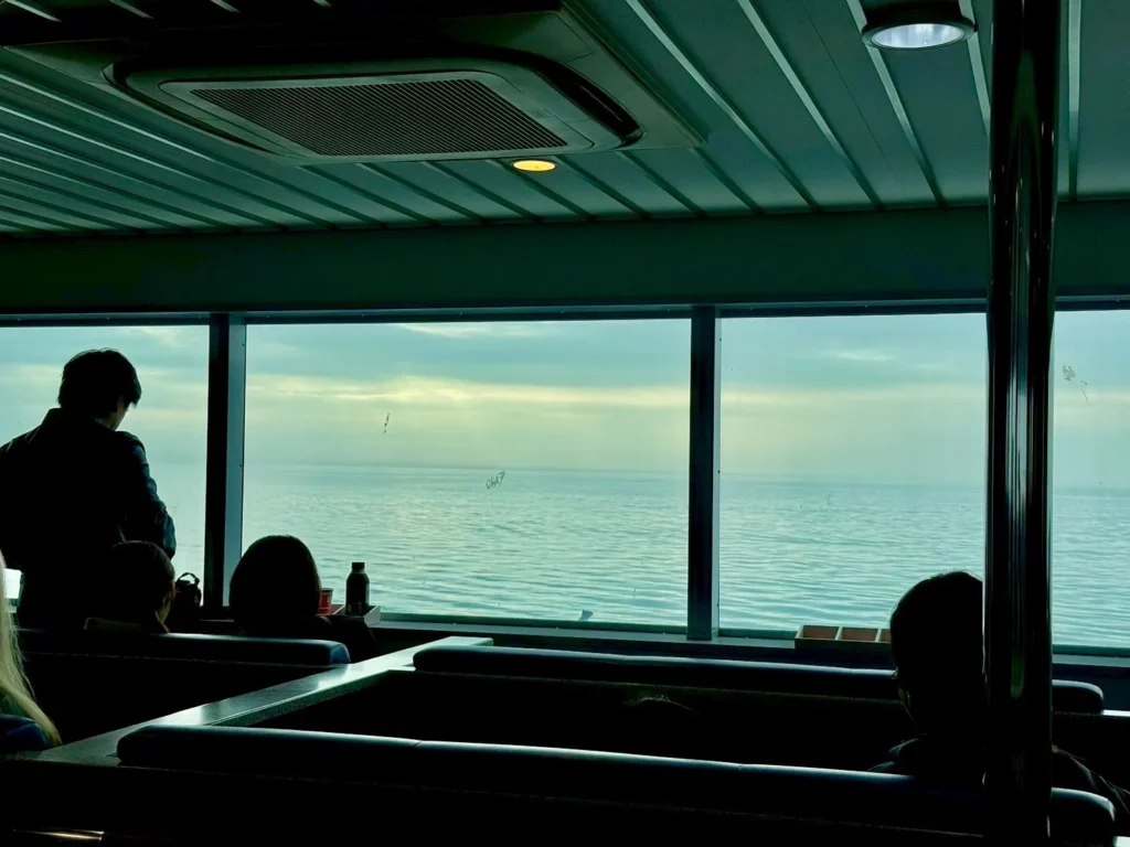 Passengers relaxing inside the Ariake Ferry lounge with panoramic windows facing the Ariake Sea