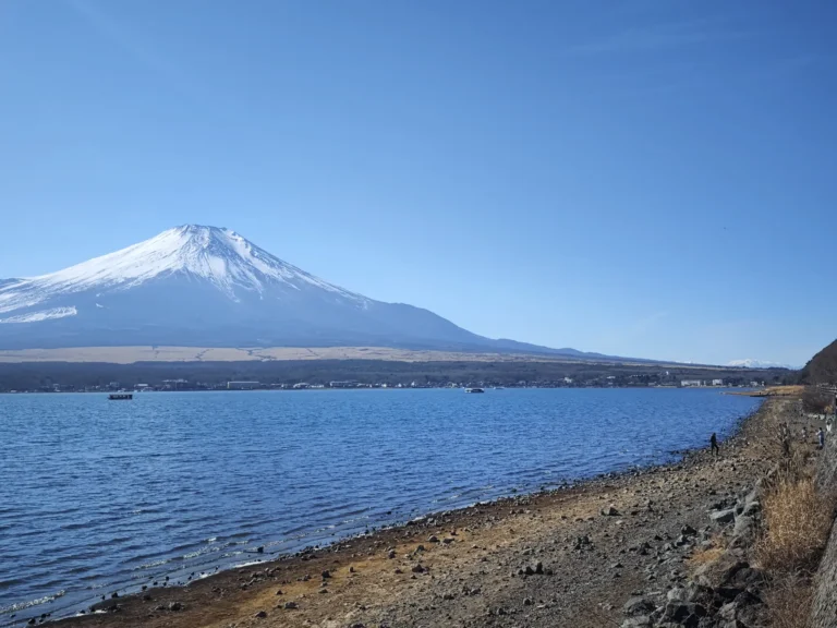 A clear, snow-capped Mount Fuji seen across Lake Yamanaka under a bright blue sky, illustrating the best conditions for Fuji visibility.