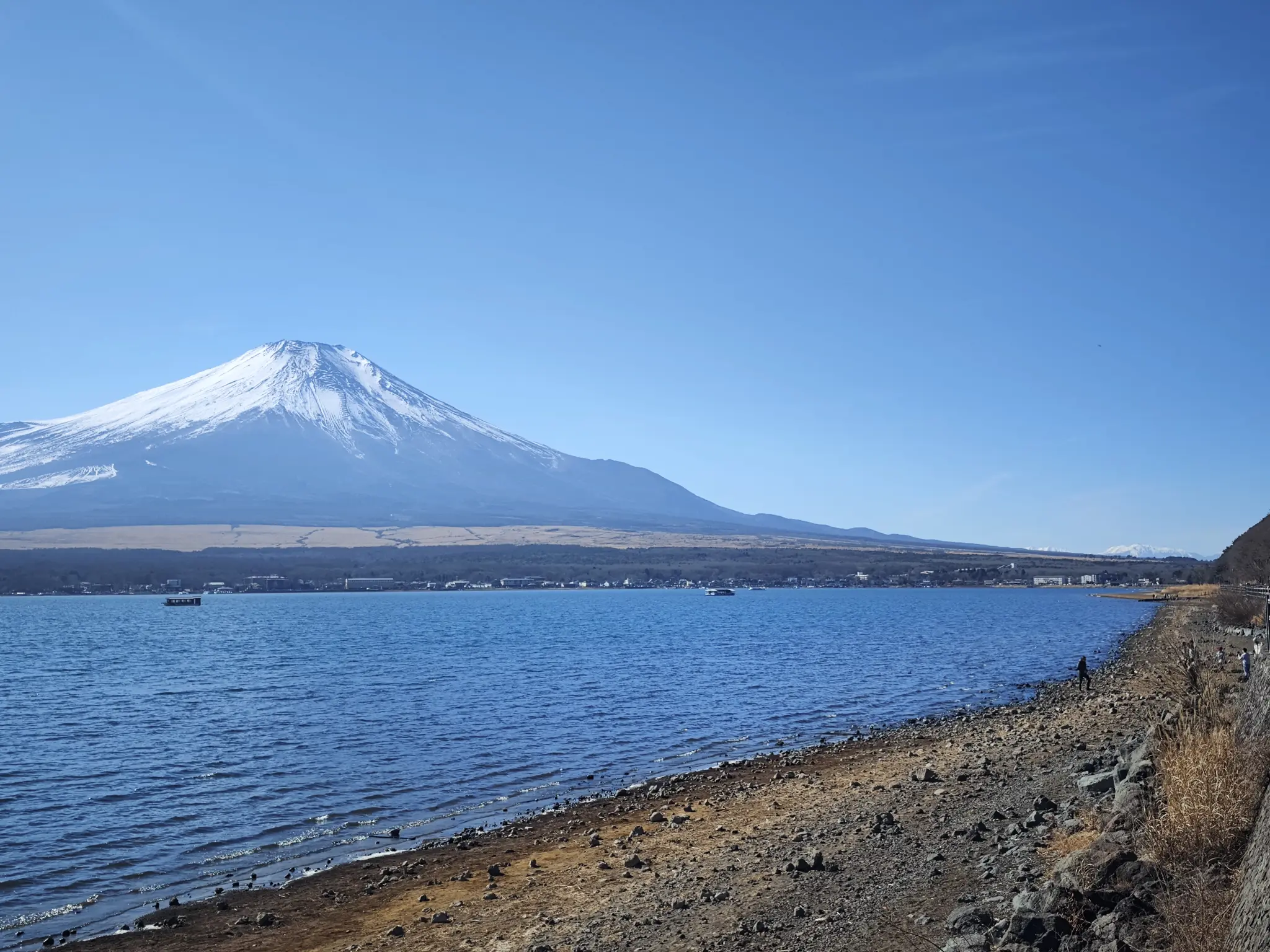 A clear, snow-capped Mount Fuji seen across Lake Yamanaka under a bright blue sky, illustrating the best conditions for Fuji visibility.