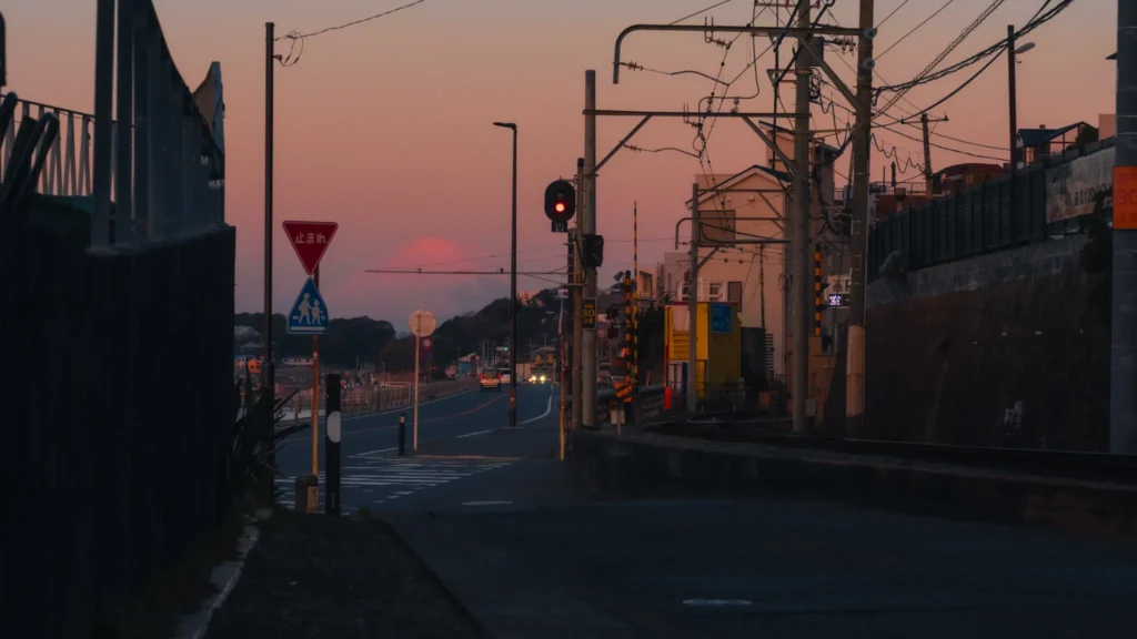 The peak of Mt. Fuji is visible in the distance down a quiet street in Shichirigahama, framed by power lines and traffic signals at dusk.