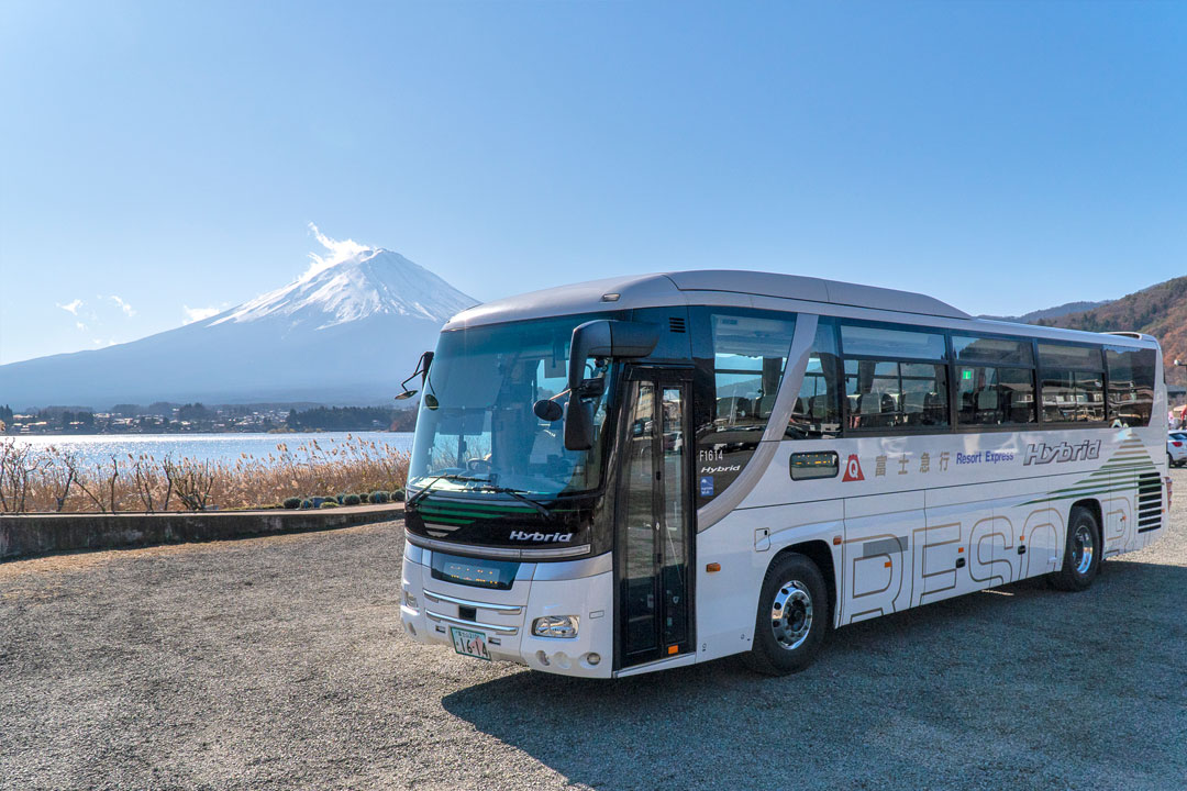 A Fujikyu Resort Express bus parked by Lake Kawaguchiko with a clear view of Mt. Fuji, illustrating how to get from Tokyo to Kawaguchiko.