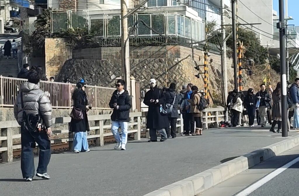A crowd of tourists gathers at the Slam Dunk crossing during the daytime, filling the sidewalks and spilling onto the road.