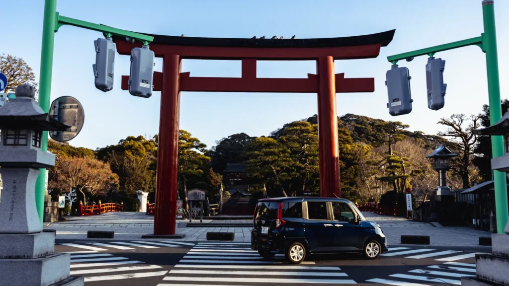 The large red San-no-Torii gate at the entrance to the shrine grounds, with a car passing in front.