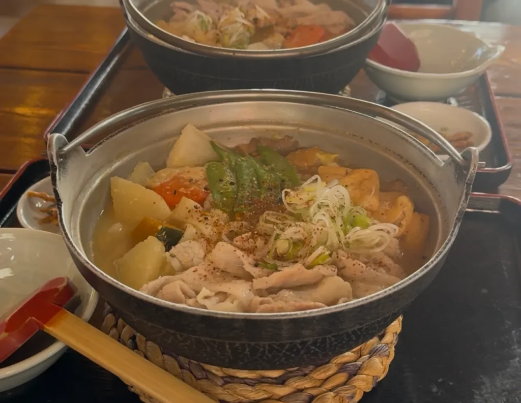 A close-up of a steaming iron pot filled with Houtou, a hearty noodle soup with pumpkin and vegetables, a perfect winter meal in Kawaguchiko.
