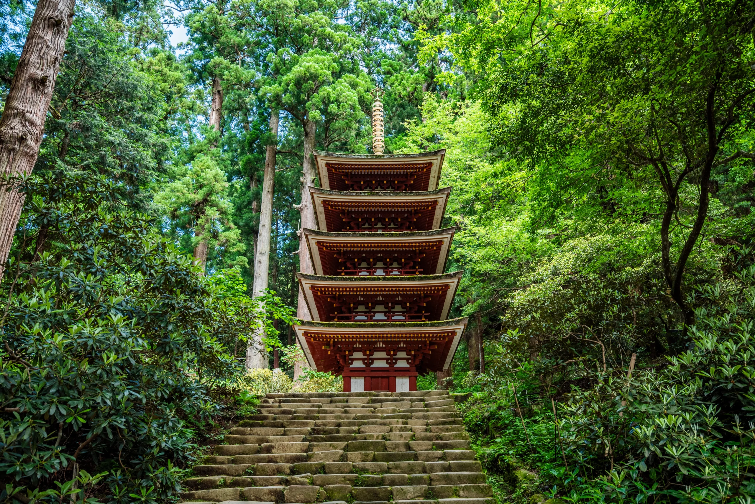 A five-storied pagoda stands tall amidst a lush green forest.