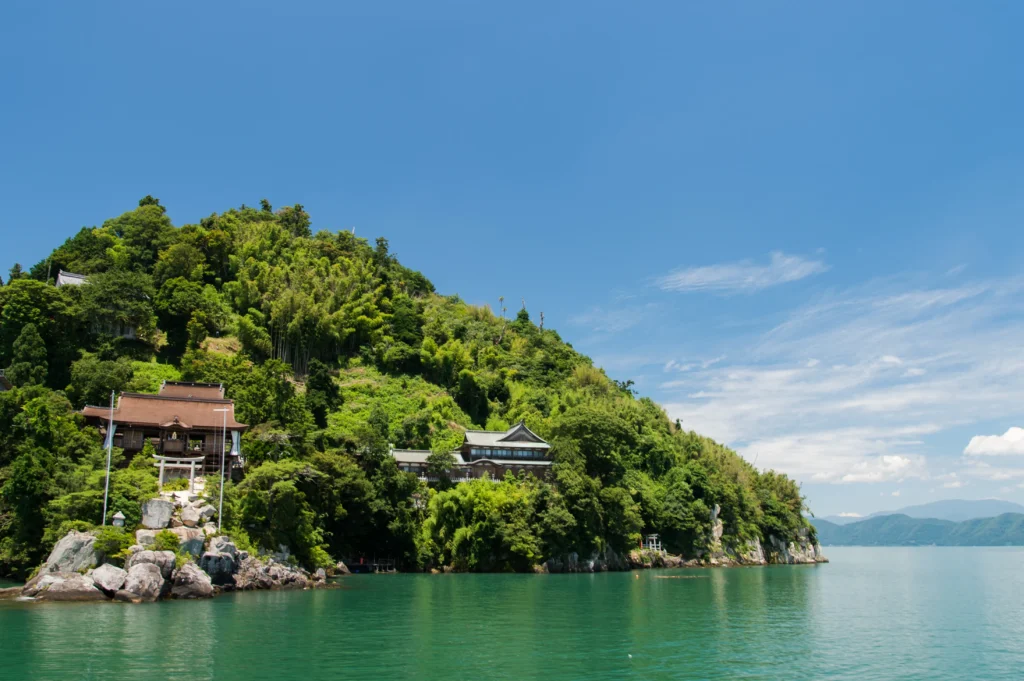 A view of a lush green island with traditional Japanese buildings on it, seen from the water.