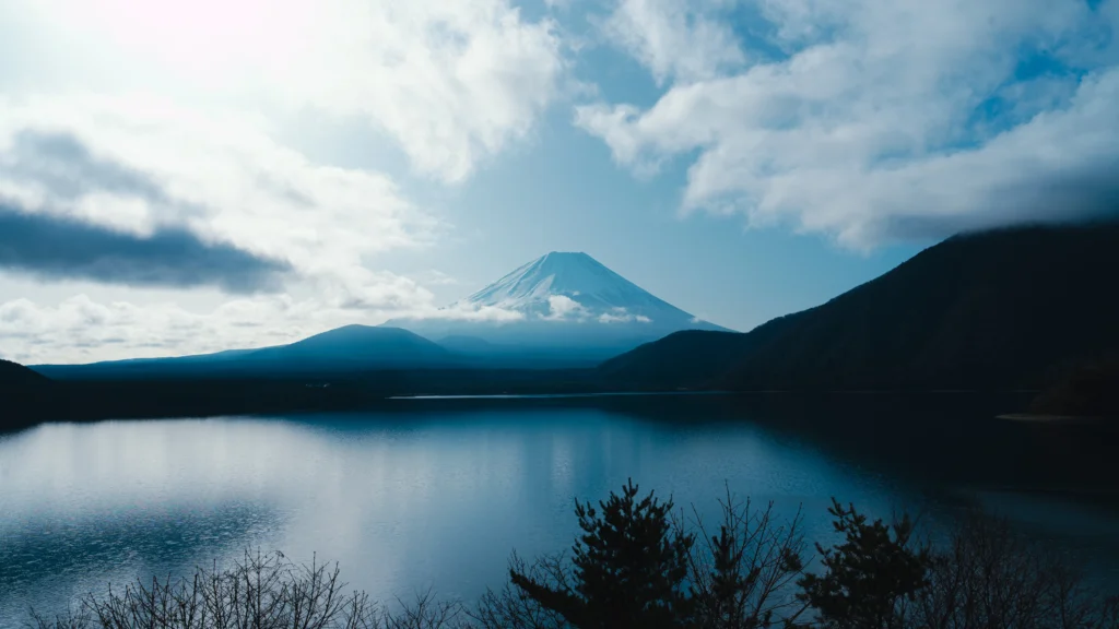 A clear, crisp view of Mount Fuji with its snow-capped peak rising above the serene, blue waters of Lake Motosu.