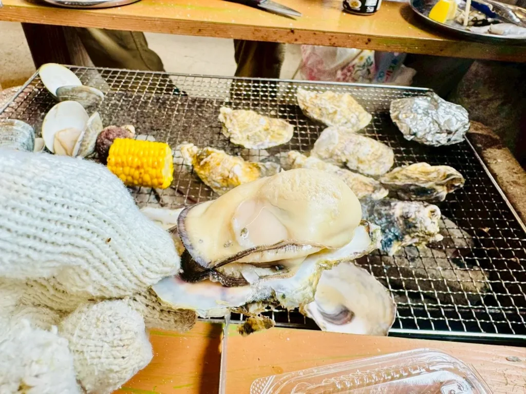 A close-up of a perfectly grilled, plump oyster, held open with a gloved hand over the grill.