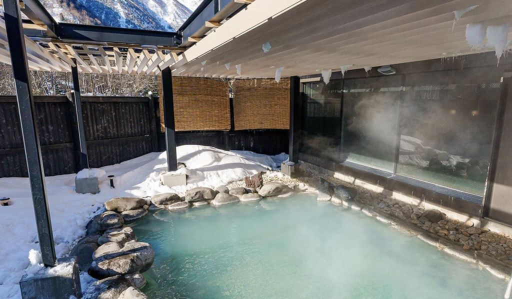 The outdoor onsen (rotenburo) at Kamenoi Hotel Oku-Nikko, with milky blue-white water steaming amidst a snowy landscape.