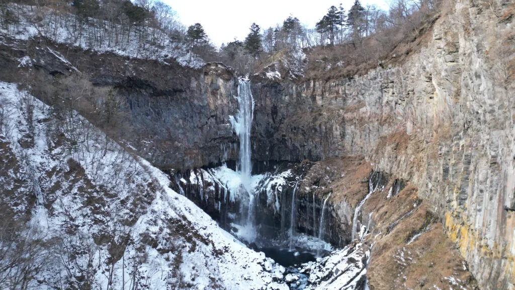 A drone shot of Kegon Falls in winter, with the main cascade surrounded by snow and ice.