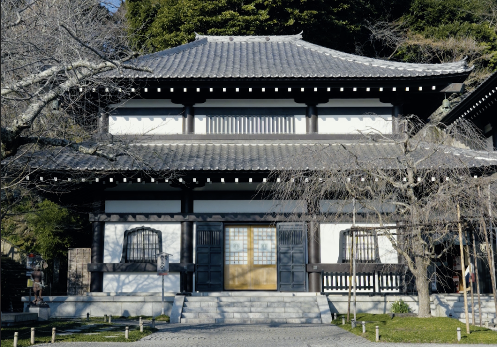 A traditional temple building at Hasedera in Kamakura with grey tile roof and golden sliding doors, surrounded by winter trees.