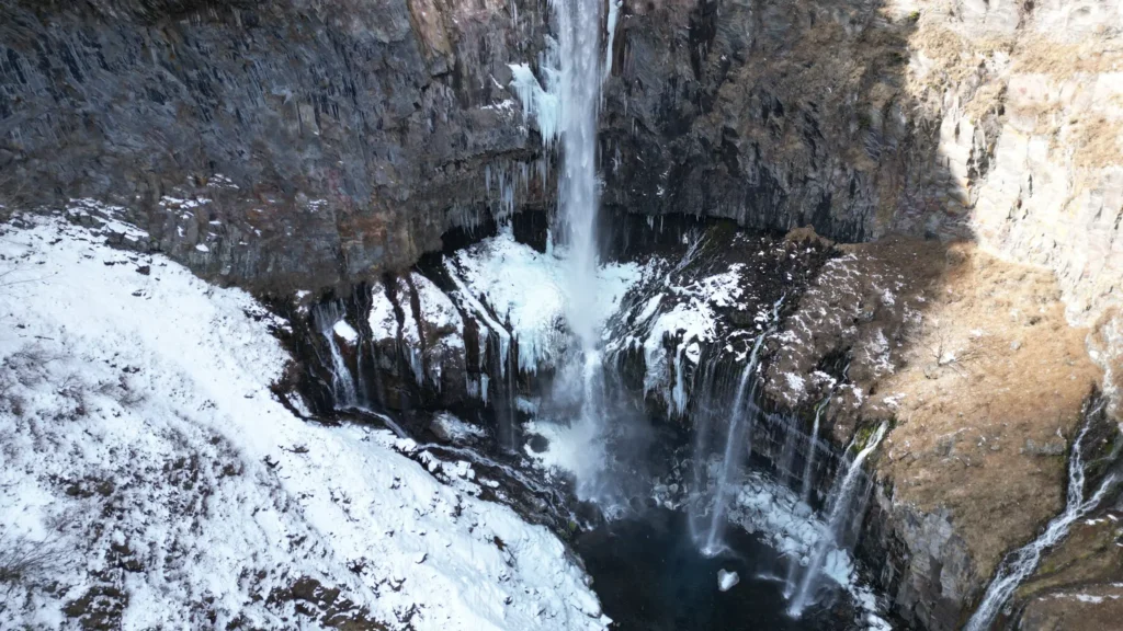Close-up aerial view of the base of Kegon Falls in winter, with icicles forming on the columnar basalt cliff face.