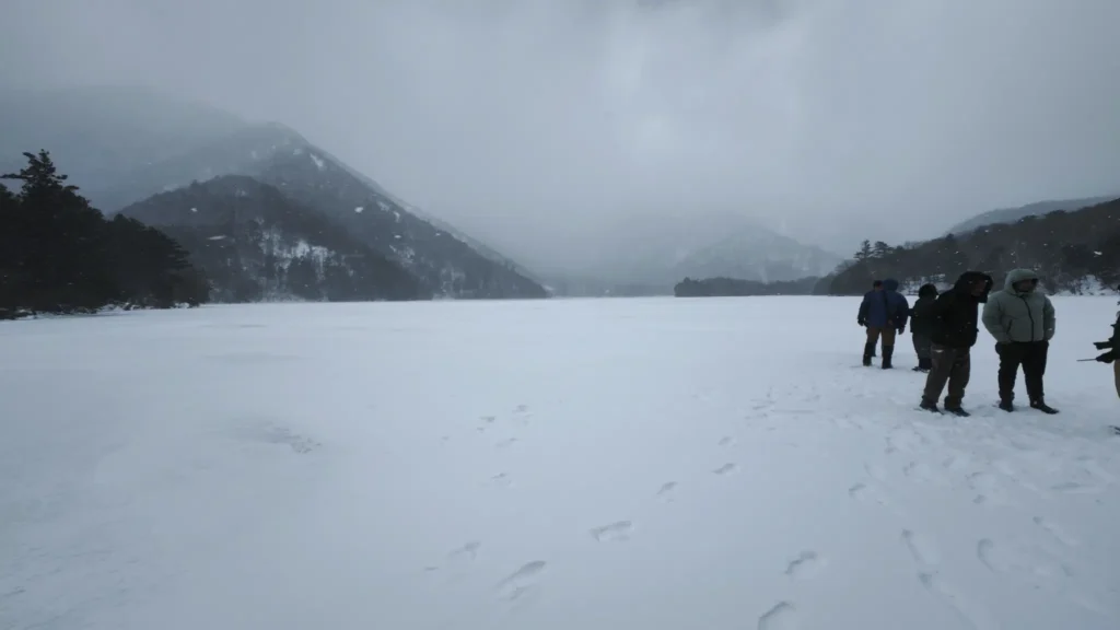 Visitors standing on the frozen and snow-covered surface of Lake Chuzenji with snow-capped mountains and mist in the background, Nikko winter.