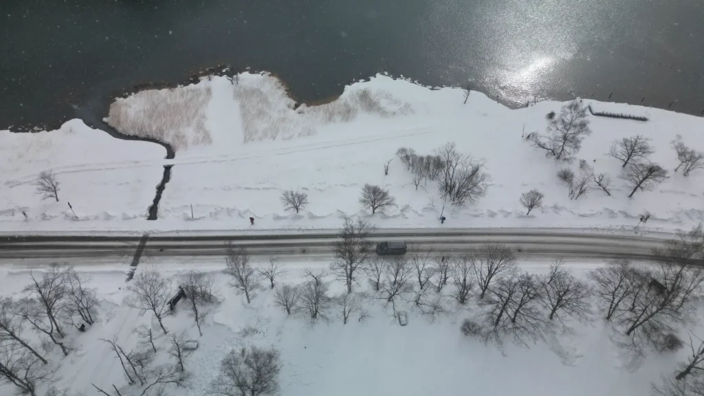 Aerial view of the road along Lake Chuzenji in winter, with a car driving on the cleared road between snow-covered banks and the partially frozen lake, Nikko.