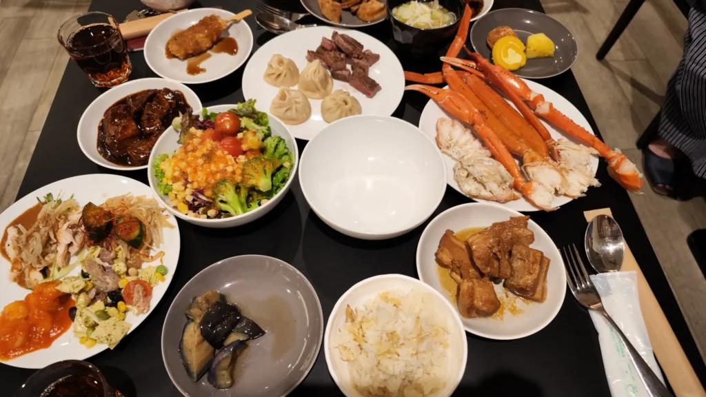 A table filled with various plates from the buffet, including crab legs, steak, dumplings, salads, and other Japanese side dishes.