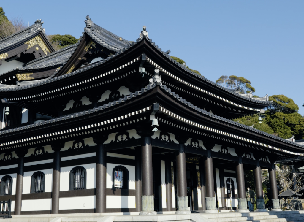The imposing Kannon-do main hall at Hasedera temple in Kamakura, featuring traditional black and white architecture with a multi-tiered roof.