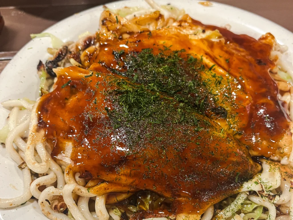 Hiroshima-style okonomiyaki with layered yakisoba noodles, egg, and otafuku sauce