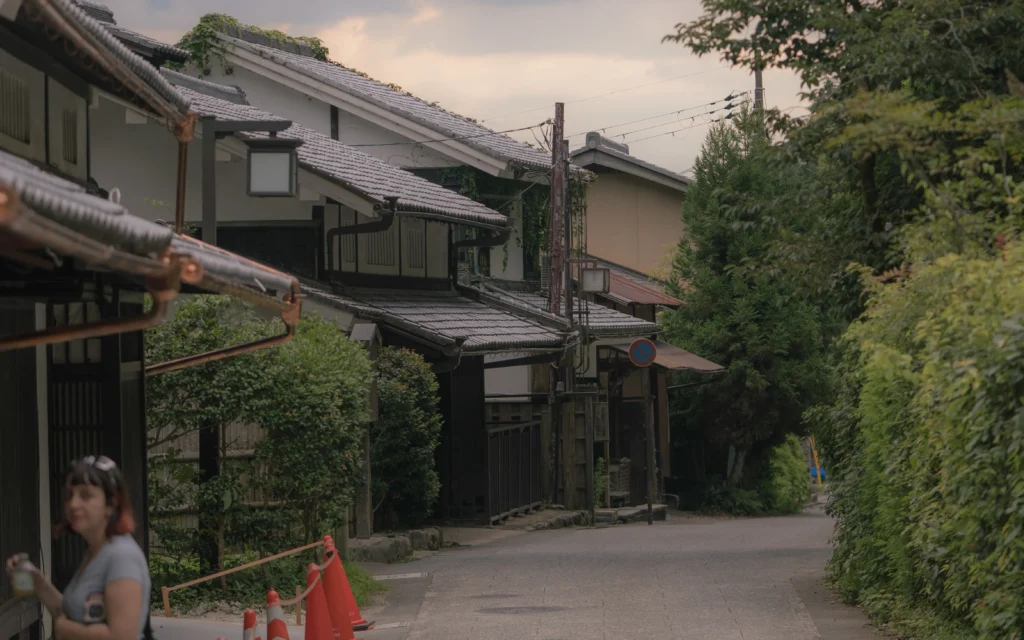 Traditional machiya townhouses with tiled roofs lining the street, evening light, a vine-covered wall on the right
