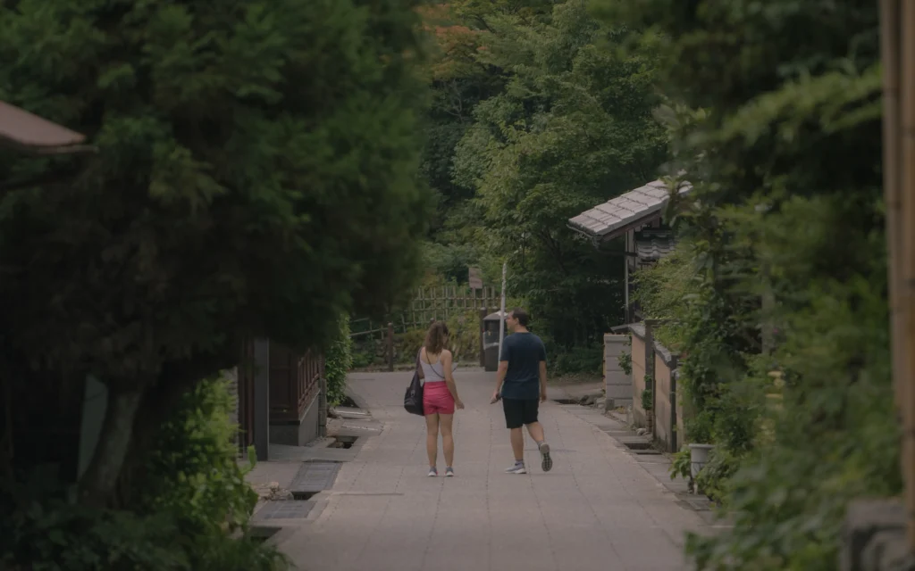 Couple walking away from camera along the preserved street with green trees and traditional buildings on both sides