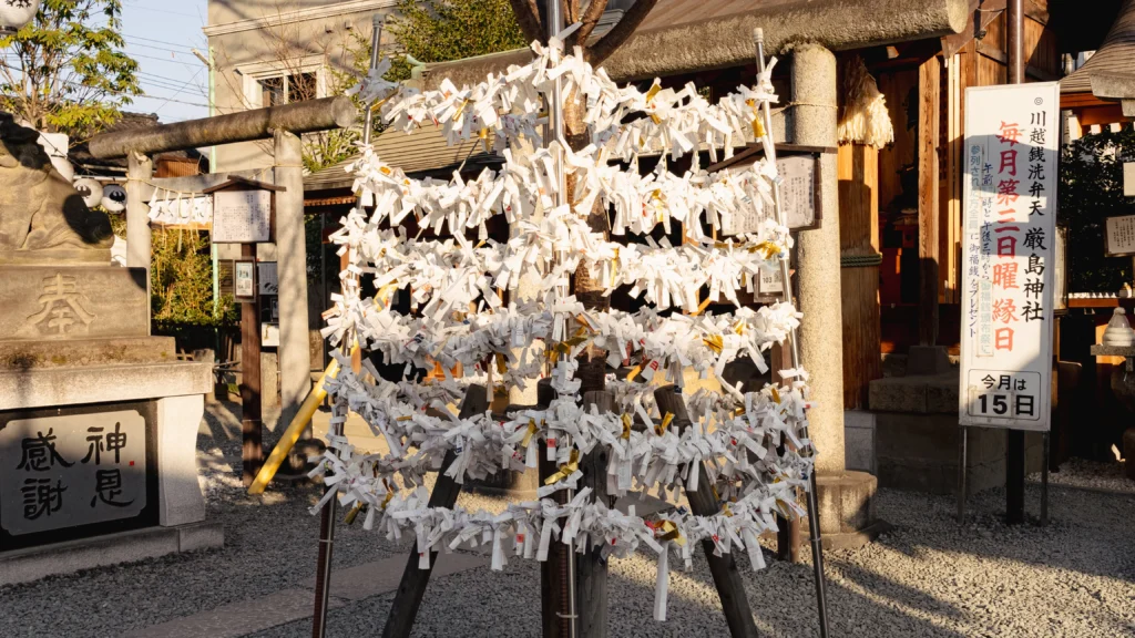 Hundreds of omikuji fortune papers tied to a tree near the Musuhi no Niwa connection garden at Kawagoe Kumano Shrine, with the Divine Gratitude stone visible