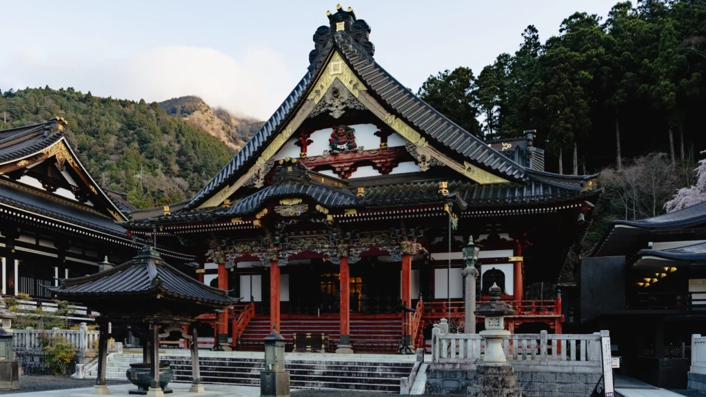 Ornate vermilion and gold Soshido hall at Minobusan Kuonji with mountain forest behind