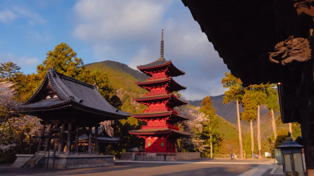 Golden hour sunlight illuminating the bell tower and pagoda at Kuonji Temple with mountains in the background