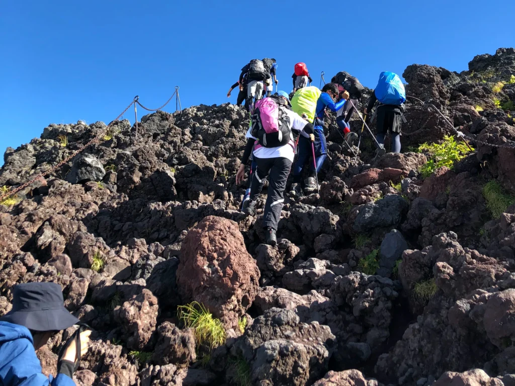 Climbers with colorful backpacks scrambling up dark volcanic rock under blue sky