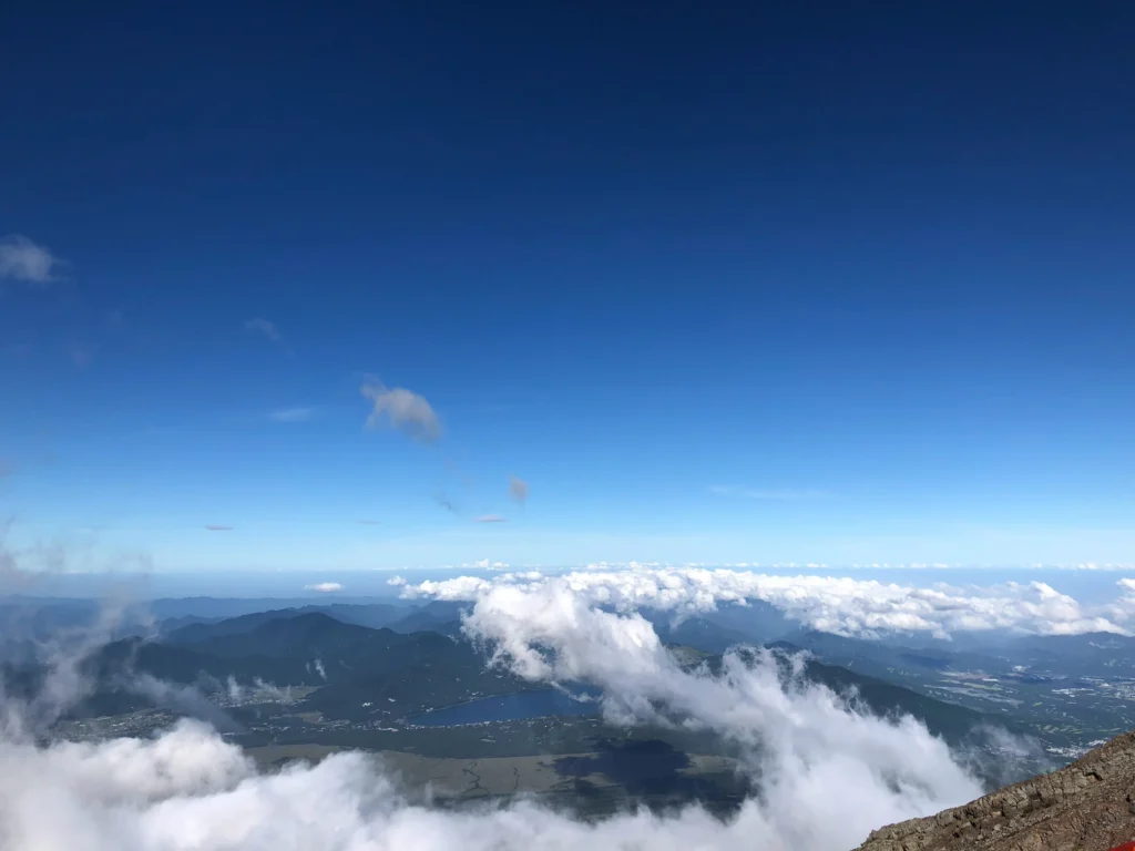 Panoramic view from summit: clouds below, blue sky, distant mountains