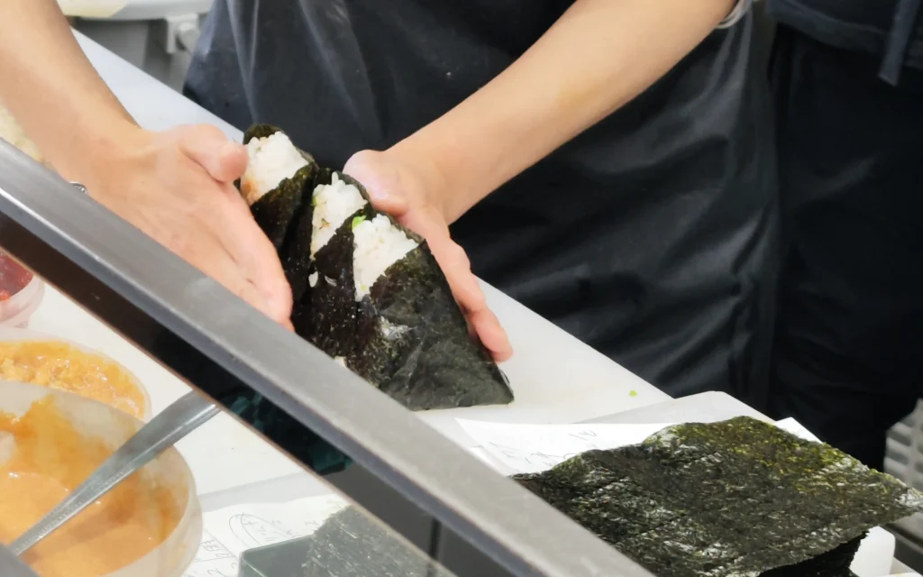Chef's hands passing freshly-made nori-wrapped onigiri to customer at Onigiri Bongo Otsuka
