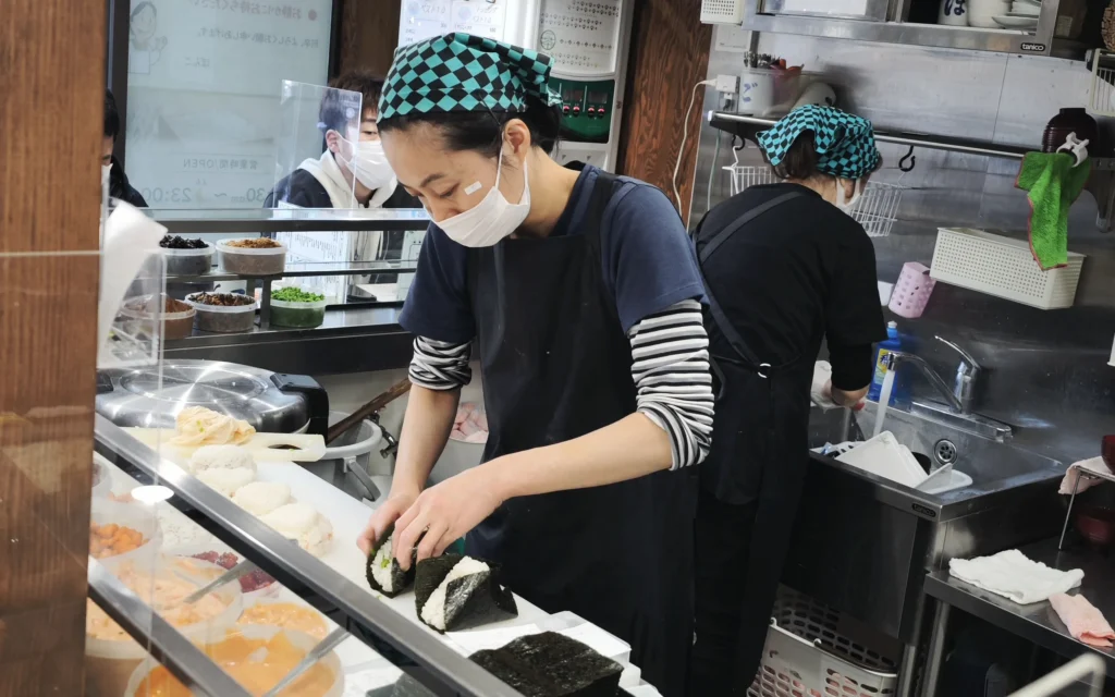 Female chef in bandana hand-shaping onigiri at Onigiri Bongo counter in Otsuka Tokyo