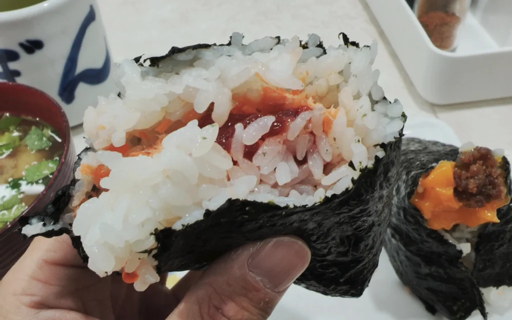 Open-bite view of Onigiri Bongo onigiri showing layers of white rice with flaked salmon and sujiko roe inside