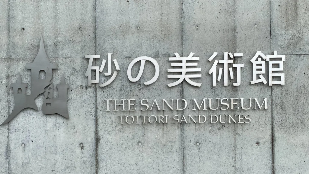 The Sand Museum entrance sign on the concrete exterior wall
