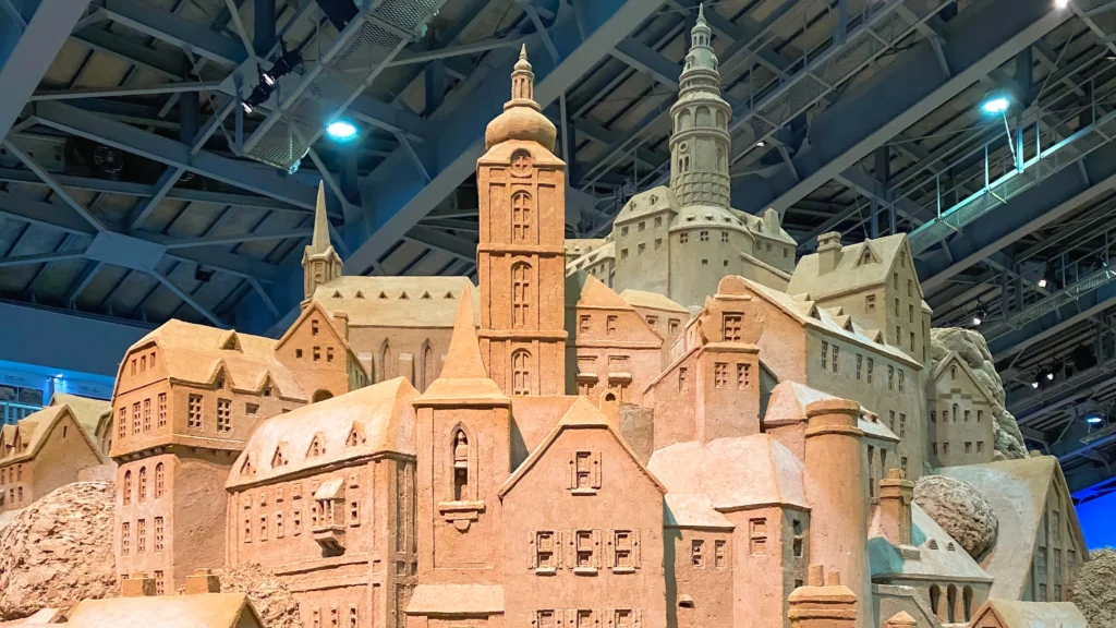 Intricate sand sculpture of a Central European cityscape with church spires and multi-story buildings