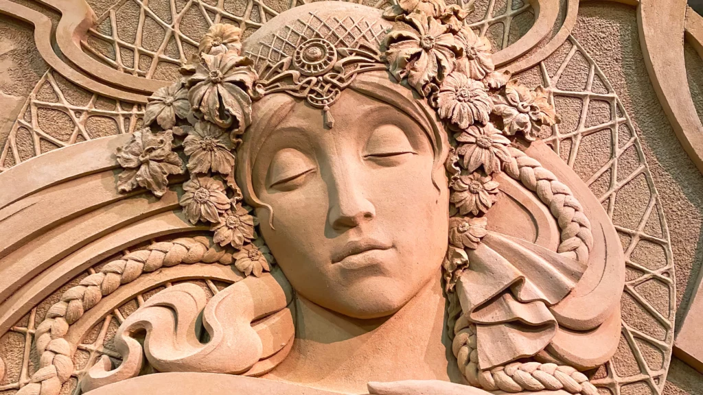 Close-up of a sand sculpture depicting a woman's face in Art Nouveau style, inspired by Alphonse Mucha
