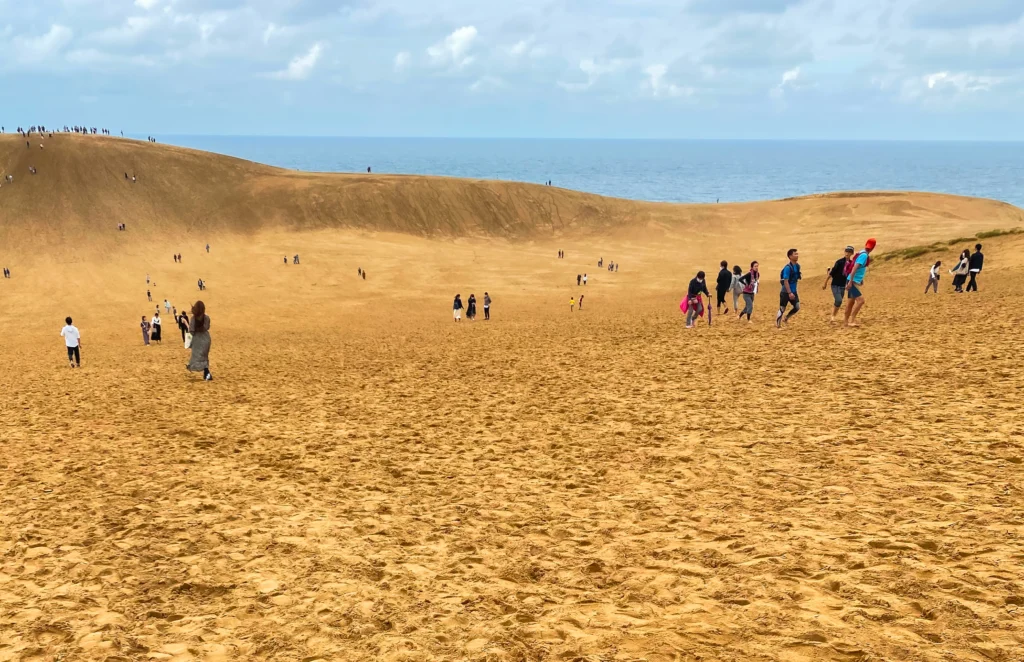 People approaching the main dune ridge with silhouettes visible along the top against the sky