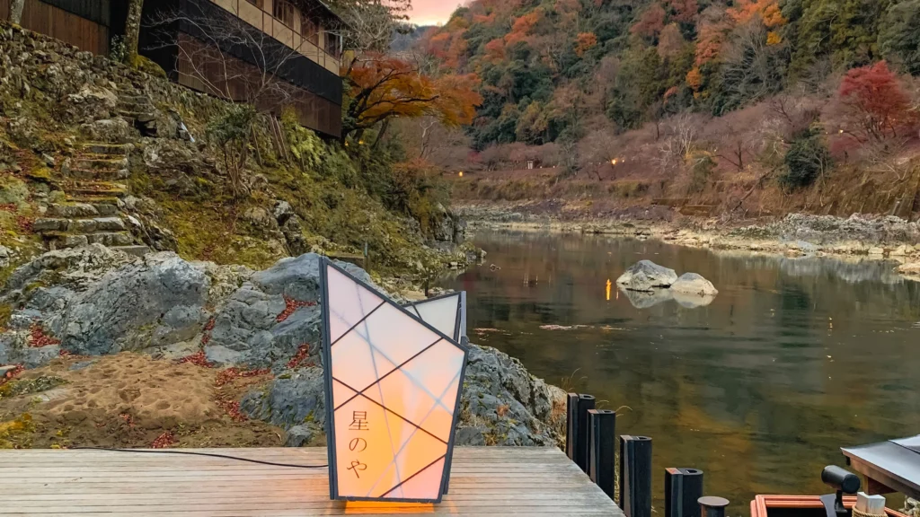 A geometric lantern illuminating a moss-covered stone dock at dusk with autumn leaves.