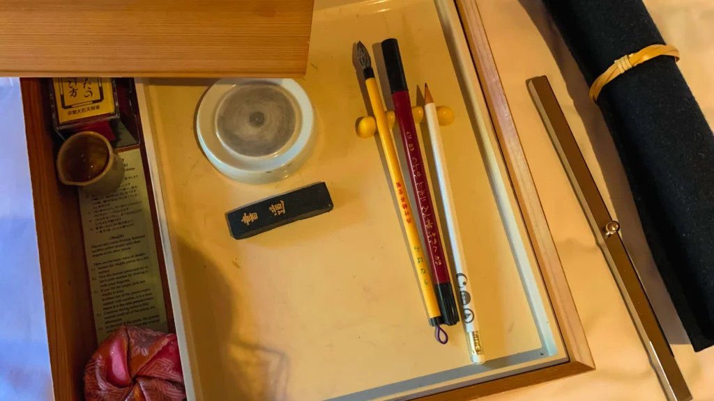 An open wooden calligraphy box containing an ink stone, an ink stick, brushes, and an instruction card.