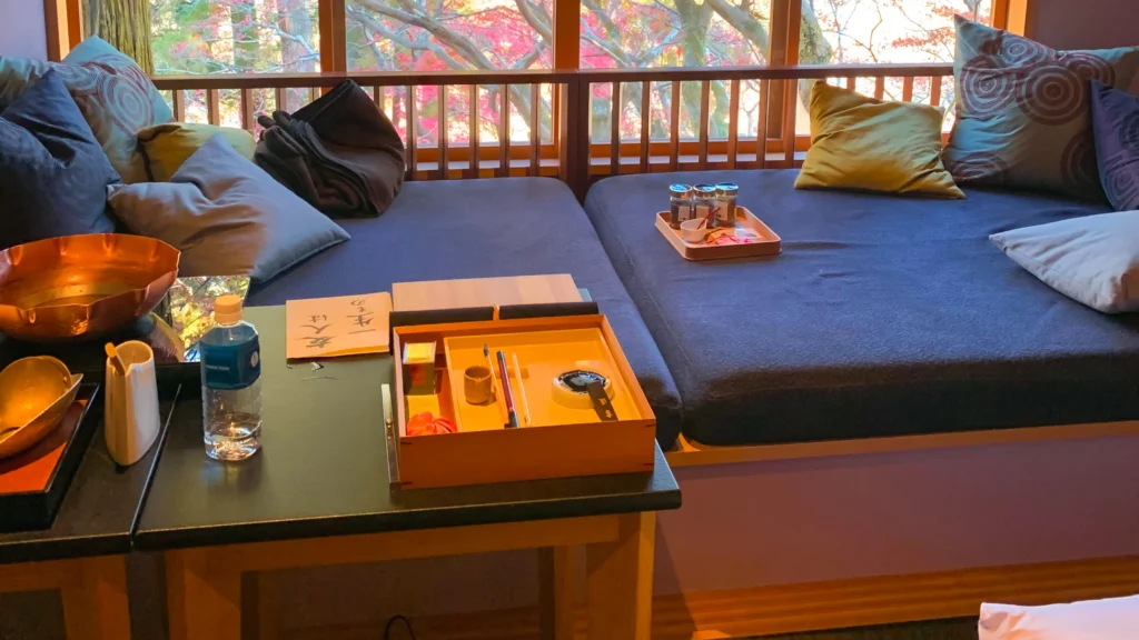 The interior of the room showing the blue daybed, a copper bowl, a calligraphy box, and the autumn windows.