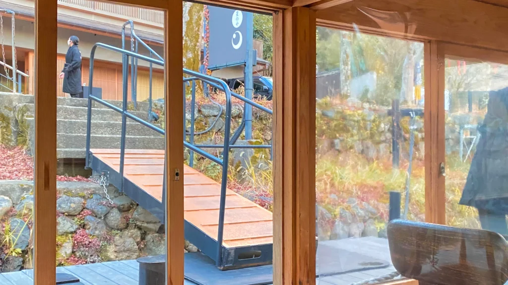 The Hoshinoya Kyoto boat waiting lounge with glass windows looking out at autumn foliage and a wooden boat dock.